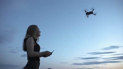 young girl controlling quadcopter drone flying in the air with remote controller under blue sky in twilight, unmanned aerial aircraft, modern technology concept