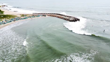 People-surfing-on-Sea-Links-Beach-shore-in-Mui-Ne,-protected-by-tetrapod-seawall