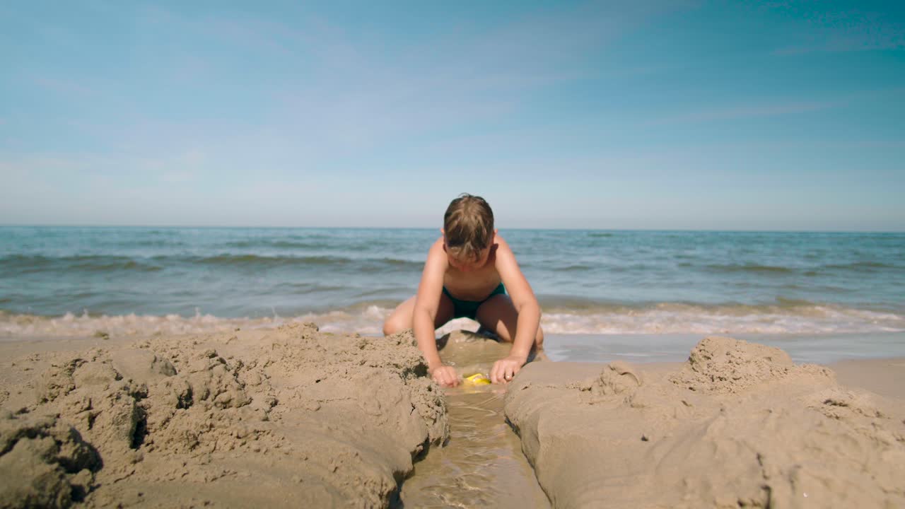 해변에서 바다를 향해 참호를 파는 어린 소년
