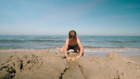 young boy digging a trench from the beach towards the ocean