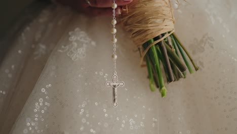 close up silver crucifix on rosary held by bride over wedding gown