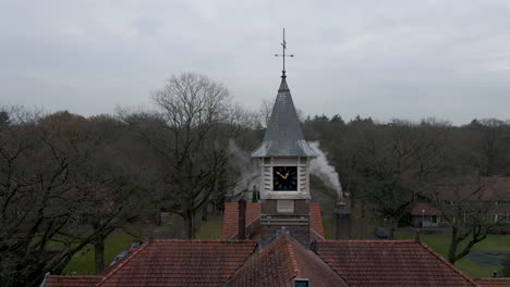 Jib-up-of-old-clocktower-overseeing-small-town-in-autumn-forest