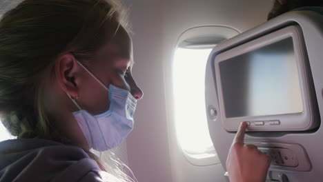 un niño con una máscara protectora usa la pantalla de entretenimiento en el avión