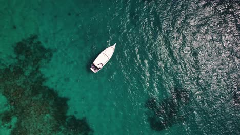 Flächenansicht-Von-Oben-Aus-Großer-Höhe-Auf-Ein-Kleines-Weißes-Boot,-Das-Im-Ruhigen-Indischen-Ozean-Auf-Den-Malediven-Parkt-Und-Die-Sonne-Auf-Der-Meeresoberfläche-Reflektiert