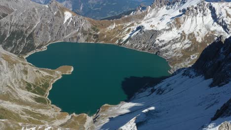 A-slow-drone-shot-going-forward-over-the-snow-and-ice-covered-mountain-peak-on-top-of-Lunersee,-overlooking-Love-Heart-Lake