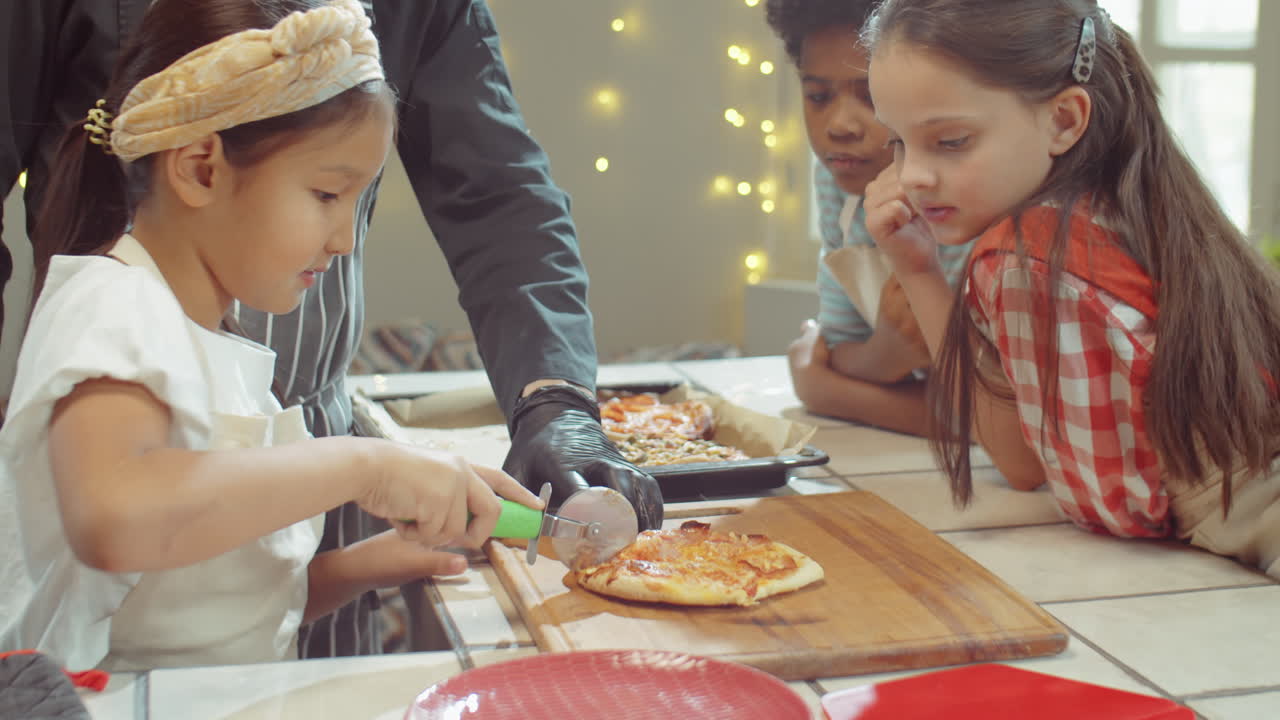Bambina asiatica piccola che taglia la pizza a una masterclass di cucina