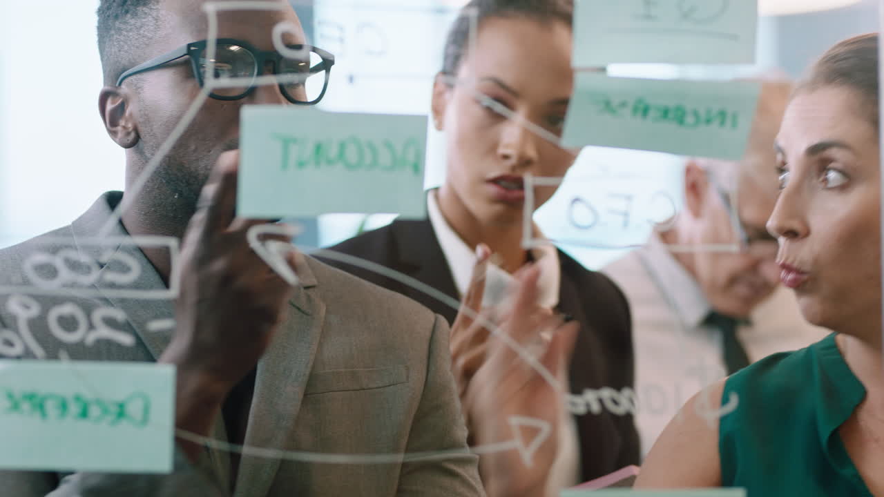 스티키 노트를 사용하는 사업가들 브레인스토밍 팀 리더 여성 동료들과 함께 유리 화이트보드에 글을 쓰고 사무실 회의에서 문제 해결 전략을 보여줍니다.