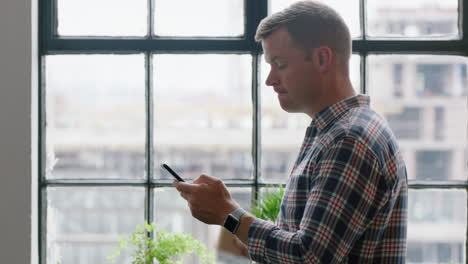 young caucasian man using smartphone drinking coffee at home enjoying relaxed morning browsing messages looking out window texting social media sharing lifestyle online close up