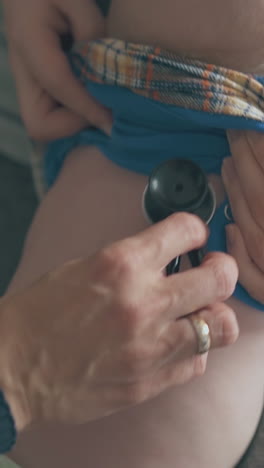young mommy helps pediatrician listen to little baby lungs and heart on bed in spacious children room at home close view