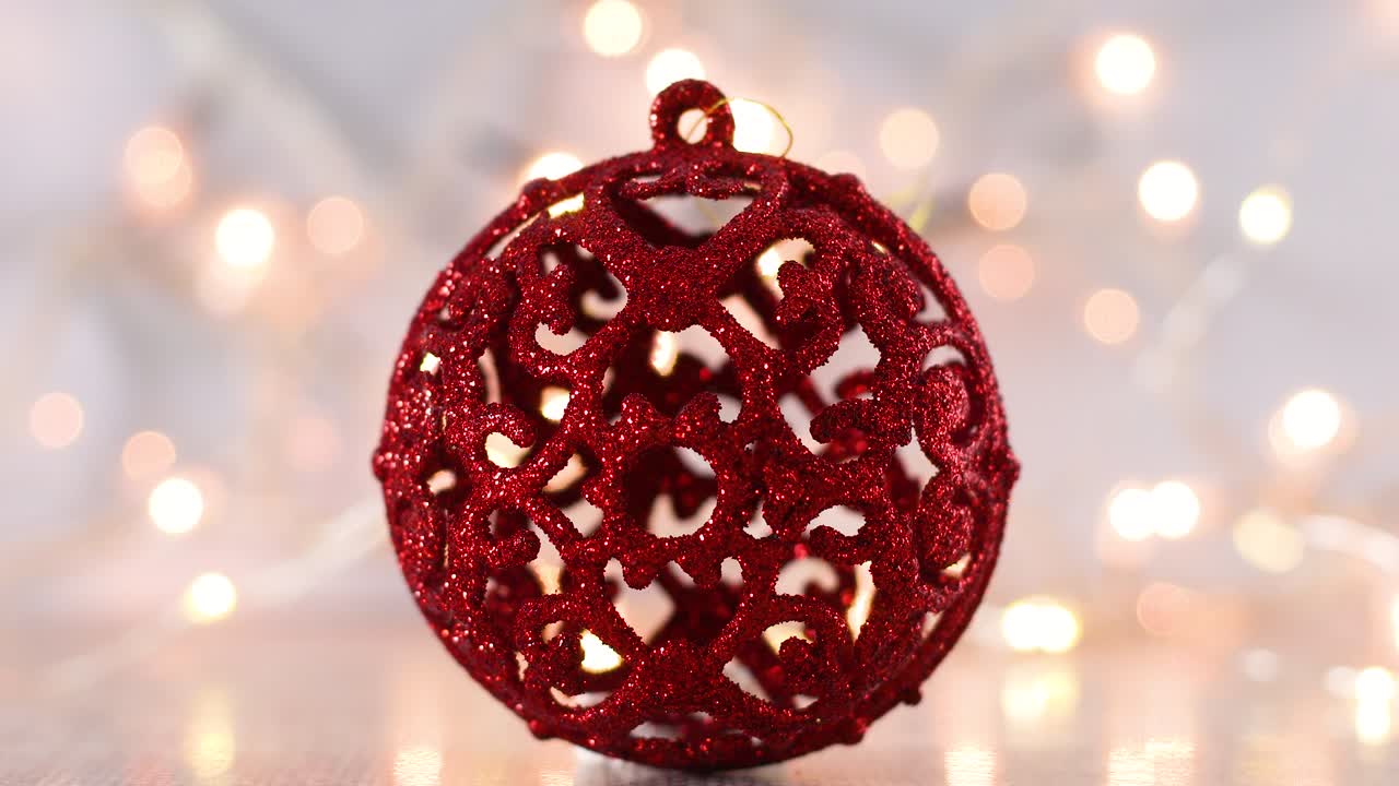 Red glitter Christmas ornament on light theme with blinking lights.