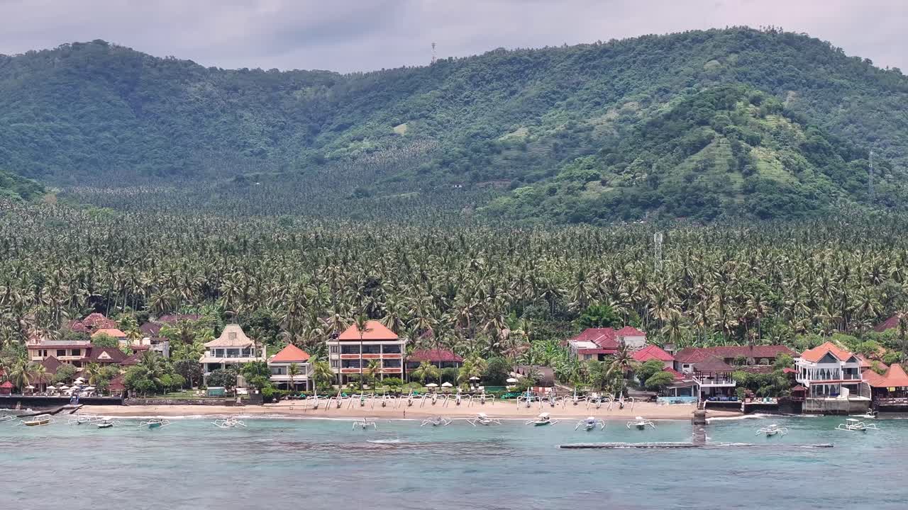 Hotels on the Candidasa Beach, palm tree plantation and mountain background. Travel Bali.