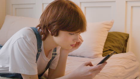 side view of girl lying on the bed and using smartphone, tapping and scrolling on the screen 2