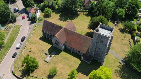 An-arc-shot-of-St-Mary's-church,-arcing-around-the-church-and-showing-the-surrounding-greenery-and-union-flag-flying-from-the-tower