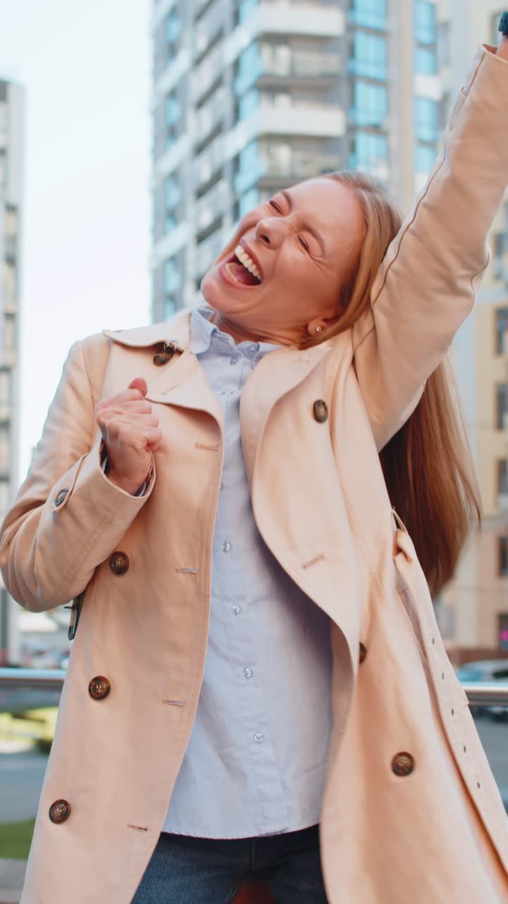 Excited woman looking surprised clenching fists shocked by sudden victory standing on city street