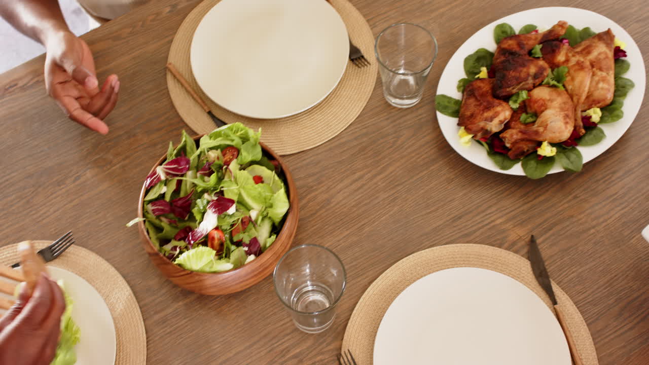 Serving fresh salad at african american family dinner table, hands preparing healthy meal