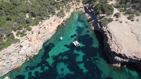 drone aerial shot view of a catamaran peacefully anchored in a turquoise cove of ibiza, basking in the sunny bliss of a perfect day at sea