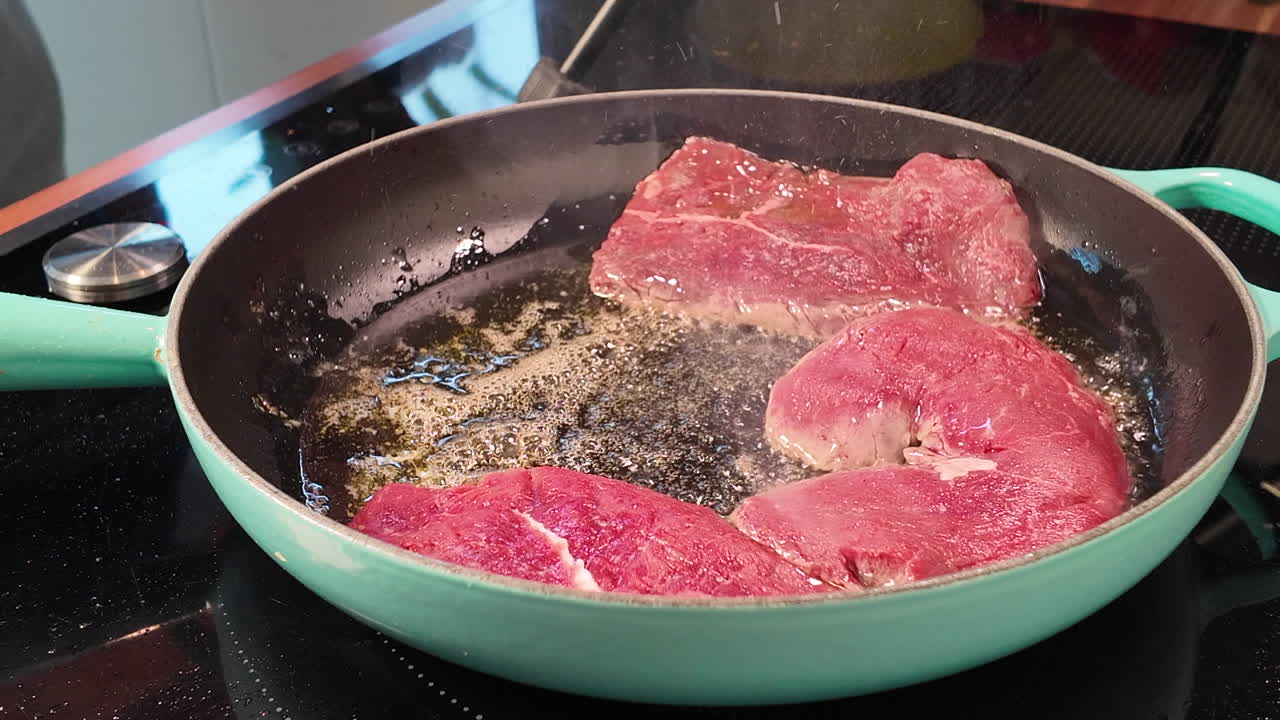 Primo piano di bistecche di manzo crude fresche che vengono messe in una padella calda con olio su un piano cottura moderno