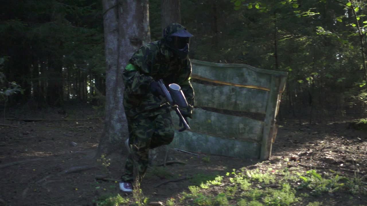 hombre jugador en juego de paintball con arma corriendo en el campo de tiro en el bosque