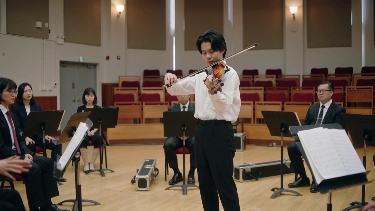 Bringing bow to strings, violinist with violin in white shirt rehearsing solo in music hall stands
