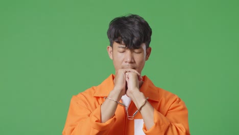 close up of asian male prisoner in handcuffs prays for something while standing on the green screen background