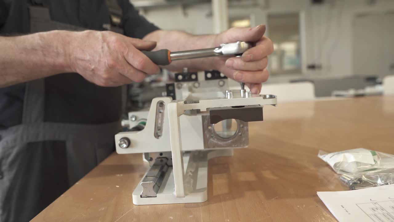 Technician tightening a bolt on a mechanical assembly. Precision hand work during equipment assembly on a workshop table