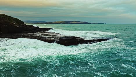 Powerful-waves-crash-up-on-rocky-ocean-shoreline-with-stunning-golden-hour-glow-in-sky