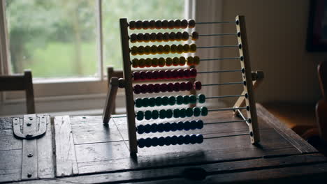 ábaco-Multicolor-Sobre-Una-Mesa-De-Madera-Desgastada,-Con-Un-Telón-De-Fondo-De-Luz-Natural-Y-Vegetación