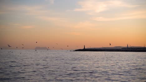 Blick-Auf-Den-Silhouettierten-Leuchtturm-Mit-Vögeln,-Die-Bei-Sonnenuntergang-Fliegen