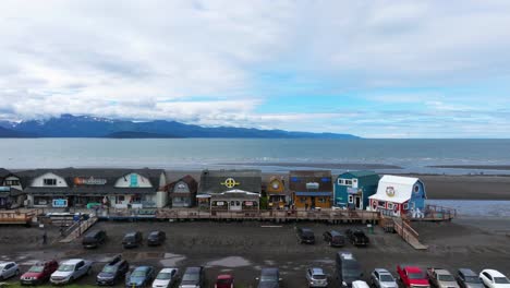 drone flyover of quaint fishing town in homer alaska, fisherman's wharf on coast line with mountain range in background