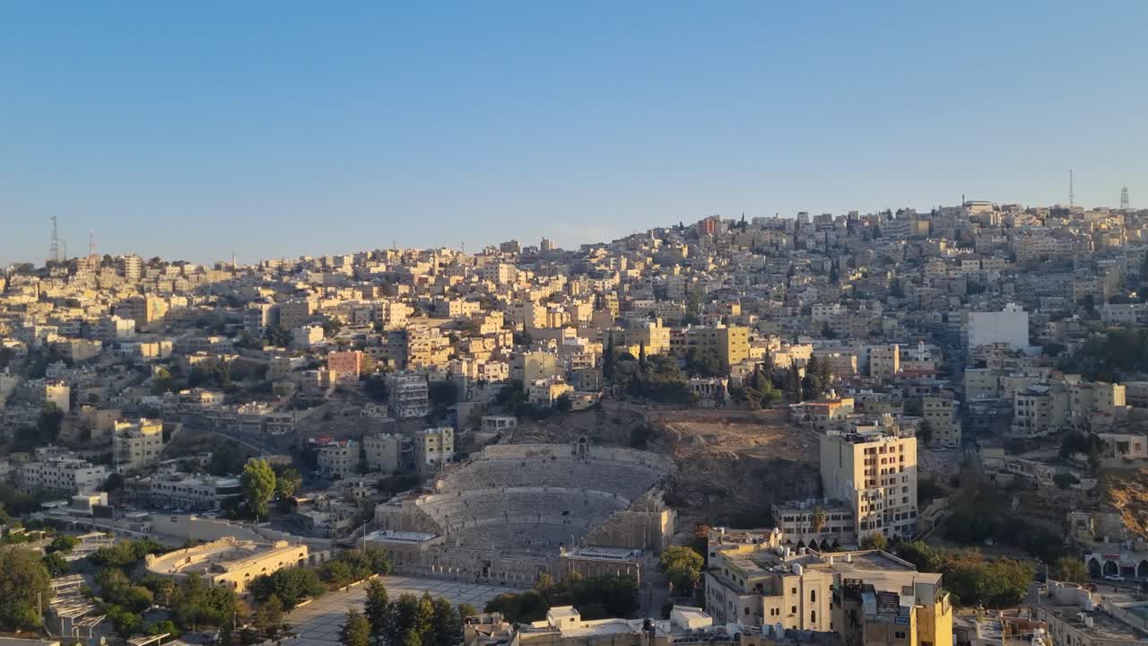 Splendida vista del tramonto su Amman, in Giordania, con le sue dolci colline e i quartieri densi che risplendono nella calda luce della sera, mentre l'antico teatro romano risalta sullo sfondo del paesaggio urbano