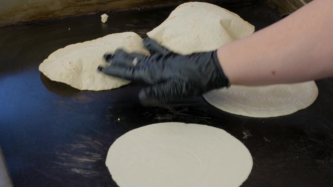 Vídeo de culinária tradicional mostrando uma senhora adicionando uma tortilla recém-feita a uma chapa durante a preparação de tortilhas de milho frescas e artesanais.