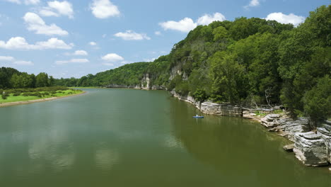 a peaceful river winds through green hills under a bright blue sky with scattered clouds