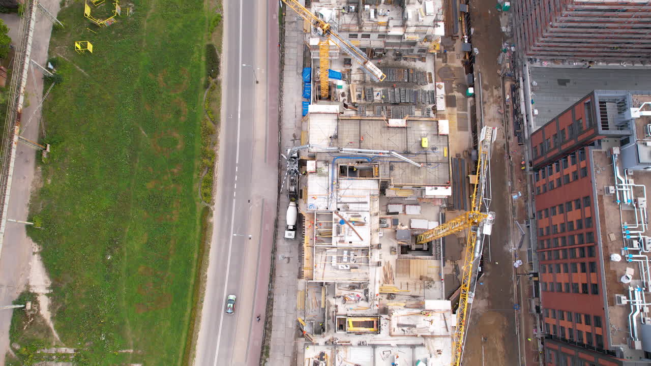 Aerial bird's eye view above busy construction site and large cranes transporting materials for high rise building