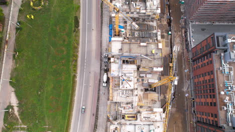 Aerial-bird's-eye-view-above-busy-construction-site-and-large-cranes-transporting-materials-for-high-rise-building