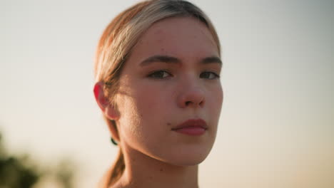 close-up of young lady with moody expression looking directly at camera under warm sunlight, conveying deep emotions, soft bokeh effect of greenery in background