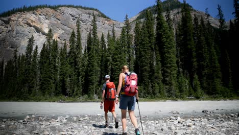 Front-view-of-young-caucasian-hiker-couple-with-backpack-hiking-near-riverside-in-the-forest-4k