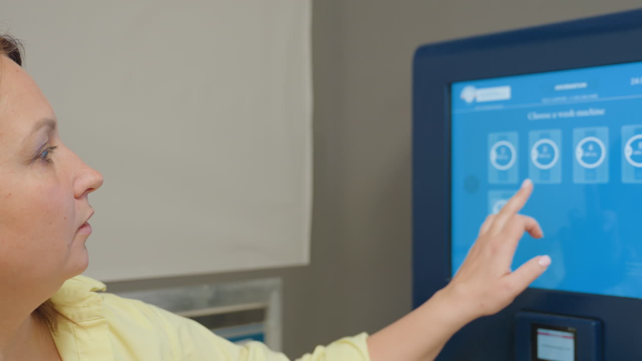 laundry owner in yellow shirt uses large blue touch screen control panel selecting washing or drying option while operating industrial machine inside modern laundromat environment