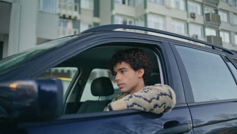 man sitting car looking window at city street closeup. young curly driver