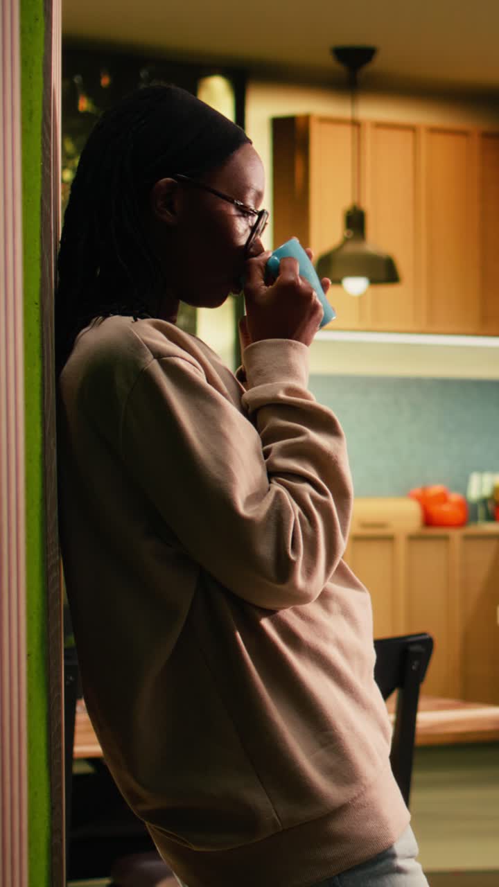 Video verticale ragazza afroamericana, che beve una tazza di caffè, che si rilassa in casa, che serve una bevanda