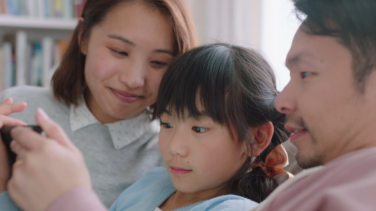 태블릿 컴퓨터를 사용하는 행복한 아시아 가족 어린 소녀는 부모와 함께 엔터테인먼트를보고 터치 스크린 장치에서 게임을하고 온라인 브라우징을하고 집에서 소파에서 함께 휴식을 취합니다 4k 영상