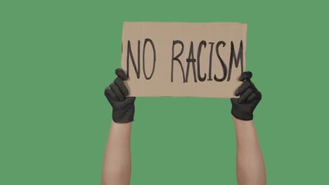 no racism. protest text message on cardboard. stop racism. police violence. banner design concept. hands in black gloves holding a poster a green screen, chroma key. close up. slow motion