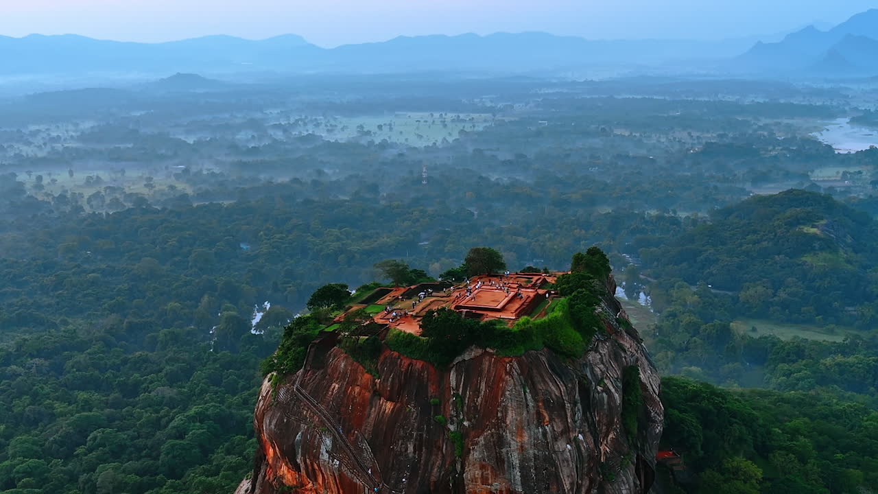 Sigiriya fortress ruins with numerous tourists walking by. Picturesque mount standing out from the hazy landscape of Sri Lanka. Aerial view.