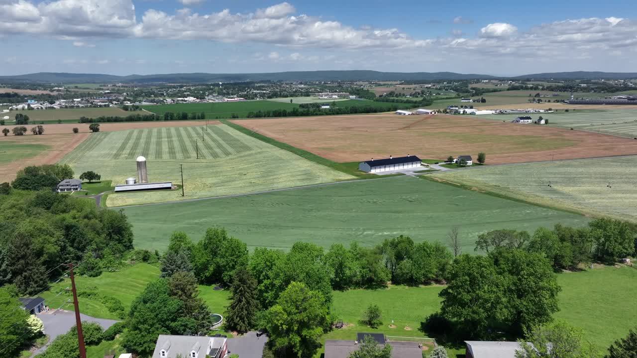 Aerial establishing shot of single family house along street in suburbia of american town. Fresh cut agricultural farm fields and farmstead in distance. Sunny spring day in May. Drone Panorama view