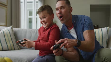 Glücklicher-Kaukasischer-Vater-Mit-Sohn,-Der-Im-Wohnzimmer-Sitzt-Und-Videospiele-Spielt