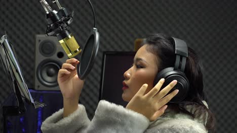 Asian-Teenager-woman-black-hair-earmuff-headphone-sing-a-song-loudly-with-power-sound-over-hanging-microphone-condenser