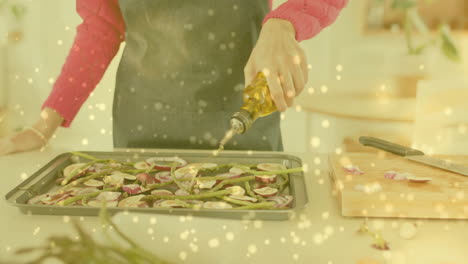 biracial woman pouring olive oil over chopped vegetables in kitchen, cooking over spots of light