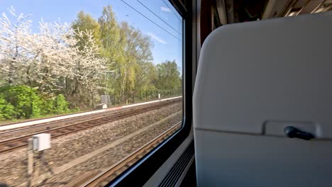 A-view-looking-out-of-a-train-window-travelling-through-the-scenic-German-countryside-between-Berlin-and-Munich-passing-a-number-of-platforms-and-stations,-Germany