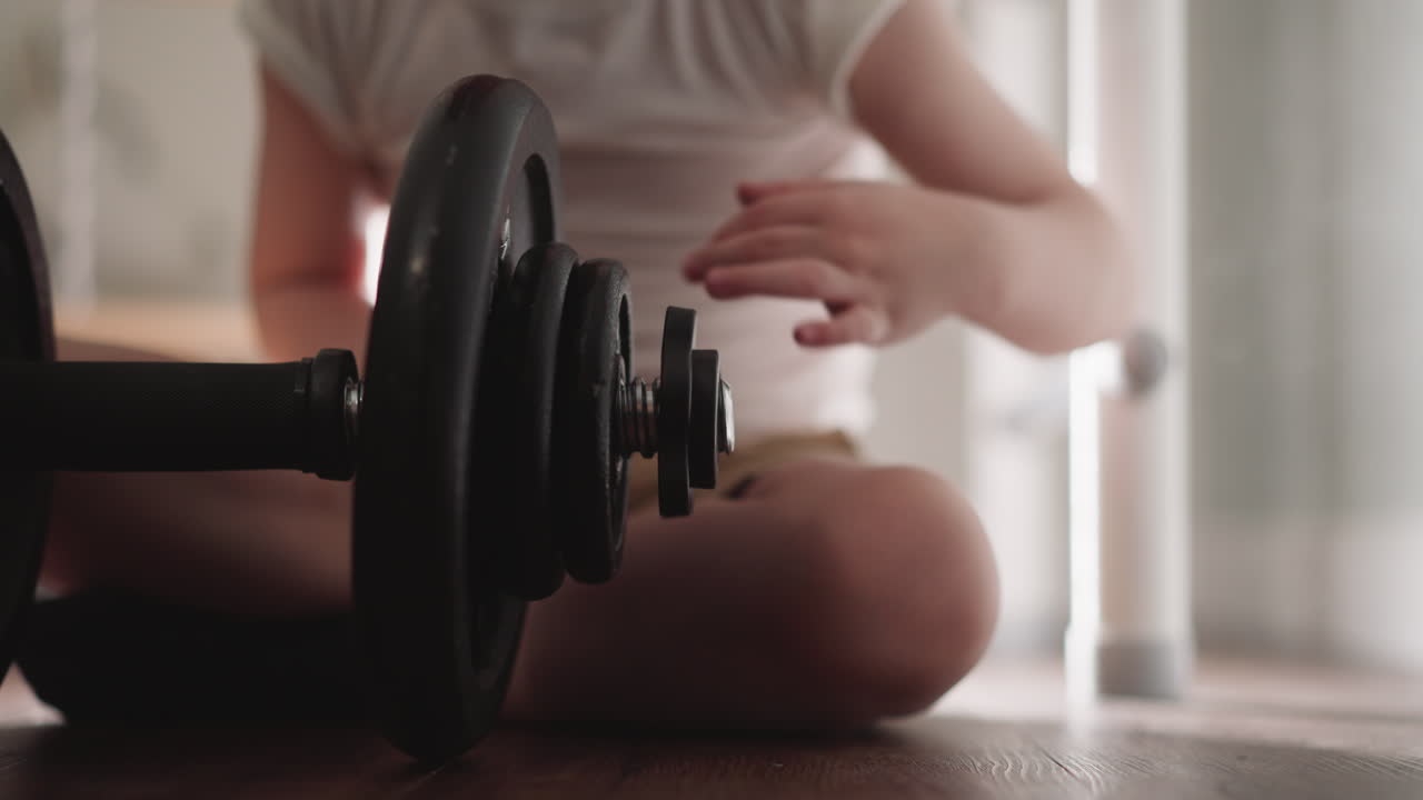 호기심 많은 소년 은 바닥 에 앉아 운동 바벨 을 다루고 있다