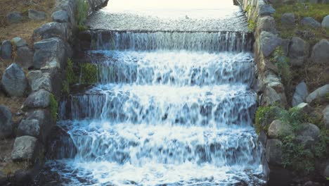 water running down from river onto rocky stairs of the waterfall