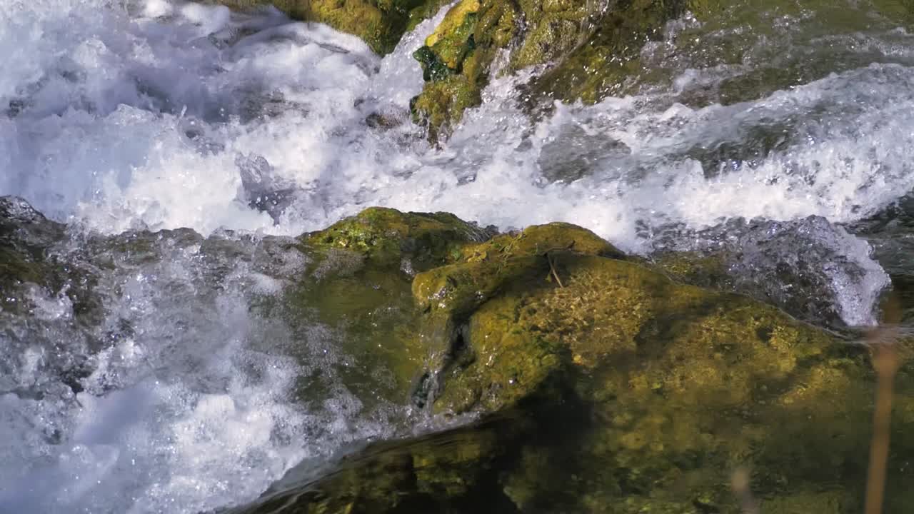 L'acqua del fiume scorre in varie direzioni mentre si fa strada a valle. Schizza in più direzioni mentre colpisce massi muschiosi sul suo percorso